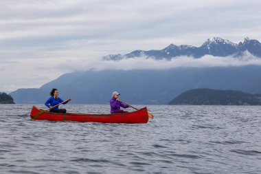 Kırmızı kano üzerinde çift maceracı kadın arkadaşlar bulutlu bir gün batımı sırasında Howe Sound kürek vardır. Bowen Adası yakınlarında çekilmiş, Vancouver'ın batısı, Bc, Kanada.
