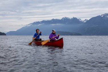 Kırmızı kano üzerinde çift maceracı kadın arkadaşlar bulutlu bir gün batımı sırasında Howe Sound kürek vardır. Bowen Adası yakınlarında çekilmiş, Vancouver'ın batısı, Bc, Kanada.