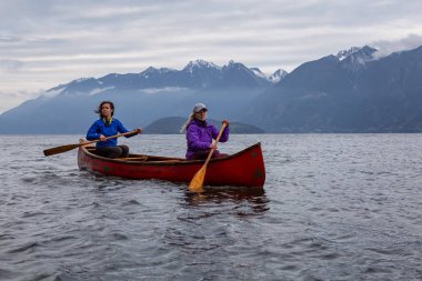 Kırmızı kano üzerinde çift maceracı kadın arkadaşlar bulutlu bir gün batımı sırasında Howe Sound kürek vardır. Bowen Adası yakınlarında çekilmiş, Vancouver'ın batısı, Bc, Kanada.