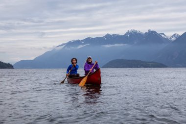 Kırmızı kano üzerinde çift maceracı kadın arkadaşlar bulutlu bir gün batımı sırasında Howe Sound kürek vardır. Bowen Adası yakınlarında çekilmiş, Vancouver'ın batısı, Bc, Kanada.