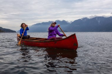 Kırmızı kano üzerinde çift maceracı kadın arkadaşlar bulutlu bir gün batımı sırasında Howe Sound kürek vardır. Bowen Adası yakınlarında çekilmiş, Vancouver'ın batısı, Bc, Kanada.