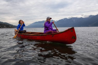 Kırmızı kano üzerinde çift maceracı kadın arkadaşlar bulutlu bir gün batımı sırasında Howe Sound kürek vardır. Bowen Adası yakınlarında çekilmiş, Vancouver'ın batısı, Bc, Kanada.