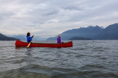 Kırmızı kano üzerinde çift maceracı kadın arkadaşlar bulutlu bir gün batımı sırasında Howe Sound kürek vardır. Horseshoe Bay, Batı Vancouver, Bc, Kanada.