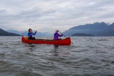 Kırmızı kano üzerinde çift maceracı kadın arkadaşlar bulutlu bir gün batımı sırasında Howe Sound kürek vardır. Horseshoe Bay, Batı Vancouver, Bc, Kanada.