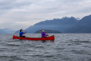 Kırmızı kano üzerinde çift maceracı kadın arkadaşlar bulutlu bir gün batımı sırasında Howe Sound kürek vardır. Horseshoe Bay, Batı Vancouver, Bc, Kanada.