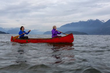 Kırmızı kano üzerinde çift maceracı kadın arkadaşlar bulutlu bir gün batımı sırasında Howe Sound kürek vardır. Horseshoe Bay, Batı Vancouver, Bc, Kanada.