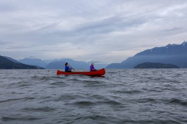 Kırmızı kano üzerinde çift maceracı kadın arkadaşlar bulutlu bir gün batımı sırasında Howe Sound kürek vardır. Horseshoe Bay, Batı Vancouver, Bc, Kanada.