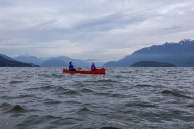 Kırmızı kano üzerinde çift maceracı kadın arkadaşlar bulutlu bir gün batımı sırasında Howe Sound kürek vardır. Horseshoe Bay, Batı Vancouver, Bc, Kanada.