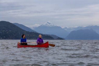 Kırmızı kano üzerinde çift maceracı kadın arkadaşlar bulutlu bir gün batımı sırasında Howe Sound kürek vardır. Horseshoe Bay, Batı Vancouver, Bc, Kanada.