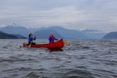 Kırmızı kano üzerinde çift maceracı kadın arkadaşlar bulutlu bir gün batımı sırasında Howe Sound kürek vardır. Horseshoe Bay, Batı Vancouver, Bc, Kanada.
