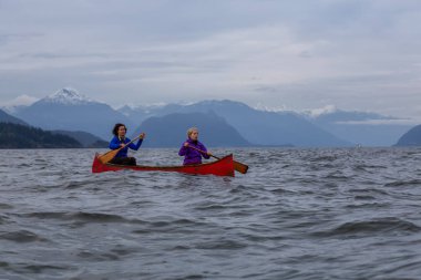 Kırmızı kano üzerinde çift maceracı kadın arkadaşlar bulutlu bir gün batımı sırasında Howe Sound kürek vardır. Horseshoe Bay, Batı Vancouver, Bc, Kanada.