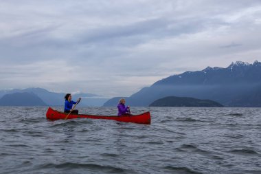 Kırmızı kano üzerinde çift maceracı kadın arkadaşlar bulutlu bir gün batımı sırasında Howe Sound kürek vardır. Horseshoe Bay, Batı Vancouver, Bc, Kanada.