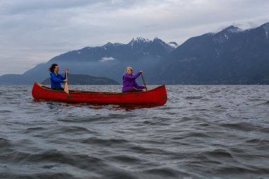 Kırmızı kano üzerinde çift maceracı kadın arkadaşlar bulutlu bir gün batımı sırasında Howe Sound kürek vardır. Horseshoe Bay, Batı Vancouver, Bc, Kanada.