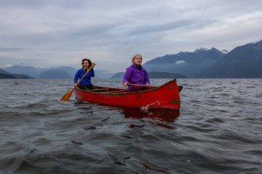 Kırmızı kano üzerinde çift maceracı kadın arkadaşlar bulutlu bir gün batımı sırasında Howe Sound kürek vardır. Horseshoe Bay, Batı Vancouver, Bc, Kanada.