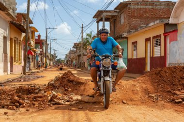 Trinidad, Küba - 08 Haziran 2019: Hareketli güneşli bir günde küçük bir Küba Kasabasının Kirli Caddesi'nde motosiklet sürmek.