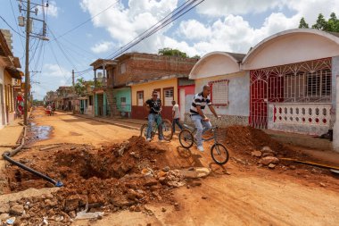 Trinidad, Küba - 08 Haziran 2019: Hareketli güneşli bir günde küçük bir Küba Kasabasının Kirli Caddesi'nde bisiklete binen Kübalılar.