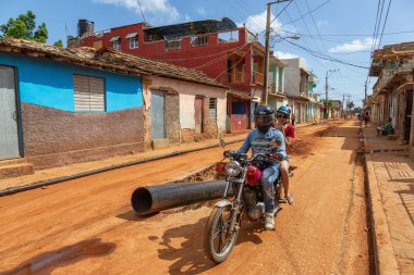 Trinidad, Küba - 08 Haziran 2019: Hareketli güneşli bir günde küçük bir Küba Kasabasının ıslak ve kirli caddesinde motosiklet sürmek.