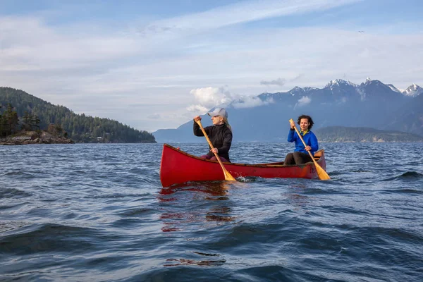 Kırmızı kano üzerinde çift maceracı kadın arkadaşlar bulutlu ve güneşli bir akşam boyunca Howe Sound kürek vardır. Bowen Adası yakınlarında çekilmiş, Vancouver'ın batısı, Bc, Kanada.
