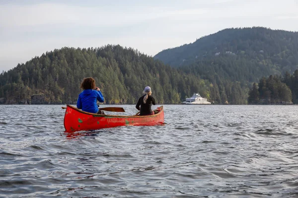 Kırmızı kano üzerinde çift maceracı kadın arkadaşlar bulutlu ve güneşli bir akşam boyunca Howe Sound kürek vardır. Bowen Adası yakınlarında çekilmiş, Vancouver'ın batısı, Bc, Kanada.