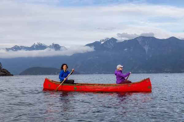 Kırmızı kano üzerinde çift maceracı kadın arkadaşlar bulutlu bir gün batımı sırasında Howe Sound kürek vardır. Bowen Adası yakınlarında çekilmiş, Vancouver'ın batısı, Bc, Kanada.