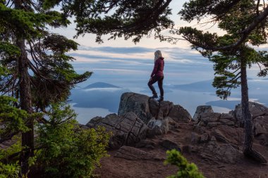 Canlı bir yaz gün batımı sırasında bulutlarla kaplı bir dağın tepesinde Kadın Hiker. St Mark Zirvesi'nin zirvesinde yer aldı, Batı Vancouver, British Columbia, Kanada.