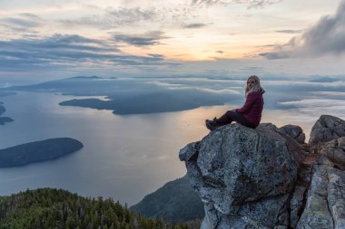 Maceracı Kadın Hiker canlı bir yaz gün batımı sırasında bulutlarla kaplı bir dağın tepesinde. St Mark Zirvesi'nin zirvesinde yer aldı, Batı Vancouver, British Columbia, Kanada.
