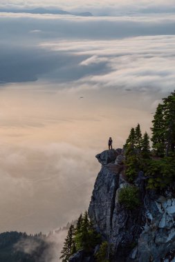 Canlı bir yaz gün batımı sırasında bulutlarla kaplı bir dağın tepesinde Kadın Hiker. St Mark Zirvesi'nin zirvesinde yer aldı, Batı Vancouver, British Columbia, Kanada.