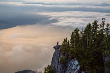 Canlı bir yaz gün batımı sırasında bulutlarla kaplı bir dağın tepesinde Kadın Hiker. St Mark Zirvesi'nin zirvesinde yer aldı, Batı Vancouver, British Columbia, Kanada.