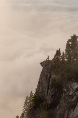 Canlı bir yaz gün batımı sırasında bulutlarla kaplı bir dağın tepesinde Kadın Hiker. St Mark Zirvesi'nin zirvesinde yer aldı, Batı Vancouver, British Columbia, Kanada.