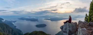 Maceracı Kadın Hiker canlı bir yaz gün batımı sırasında bulutlarla kaplı bir dağın tepesinde. St Mark Zirvesi'nin zirvesinde yer aldı, Batı Vancouver, British Columbia, Kanada.