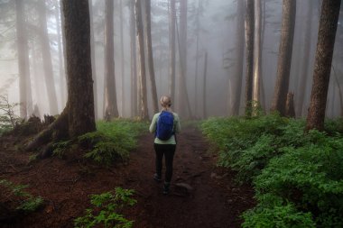 Maceracı bir kız sisli ve yağmurlu bir gün boyunca ormanda bir iz üzerinde yürüyüş. Alınan Cypress Provincial Park, Vancouver, British Columbia, Kanada.