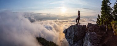 Maceracı Kadın Hiker canlı bir yaz gün batımı sırasında bulutlarla kaplı bir dağın tepesinde. St Mark Zirvesi'nin zirvesinde yer aldı, Batı Vancouver, British Columbia, Kanada.