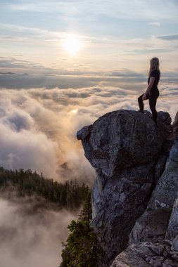 Maceracı Kadın Hiker canlı bir yaz gün batımı sırasında bulutlarla kaplı bir dağın tepesinde. St Mark Zirvesi'nin zirvesinde yer aldı, Batı Vancouver, British Columbia, Kanada.