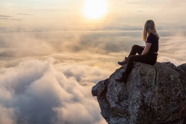 Maceracı Kadın Hiker canlı bir yaz gün batımı sırasında bulutlarla kaplı bir dağın tepesinde. St Mark Zirvesi'nin zirvesinde yer aldı, Batı Vancouver, British Columbia, Kanada.