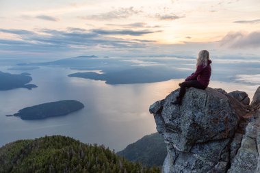 Maceracı Kadın Hiker canlı bir yaz gün batımı sırasında bulutlarla kaplı bir dağın tepesinde. St Mark Zirvesi'nin zirvesinde yer aldı, Batı Vancouver, British Columbia, Kanada.
