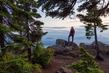 Canlı bir yaz gün batımı sırasında bulutlarla kaplı bir dağın tepesinde Kadın Hiker. St Mark Zirvesi'nin zirvesinde yer aldı, Batı Vancouver, British Columbia, Kanada.