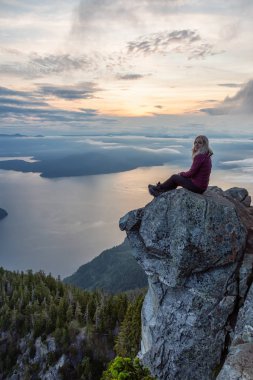 Maceracı Kadın Hiker canlı bir yaz gün batımı sırasında bulutlarla kaplı bir dağın tepesinde. St Mark Zirvesi'nin zirvesinde yer aldı, Batı Vancouver, British Columbia, Kanada.
