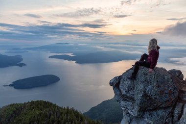Maceracı Kadın Hiker canlı bir yaz gün batımı sırasında bulutlarla kaplı bir dağın tepesinde. St Mark Zirvesi'nin zirvesinde yer aldı, Batı Vancouver, British Columbia, Kanada.