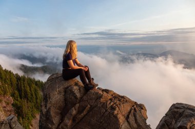 Maceracı Kadın Hiker canlı bir yaz gün batımı sırasında bulutlarla kaplı bir dağın tepesinde. St Mark Zirvesi'nin zirvesinde yer aldı, Batı Vancouver, British Columbia, Kanada.
