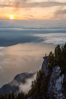 Canlı bir yaz gün batımı sırasında bulutlarla kaplı bir dağın tepesinde Kadın Hiker. St Mark Zirvesi'nin zirvesinde yer aldı, Batı Vancouver, British Columbia, Kanada.