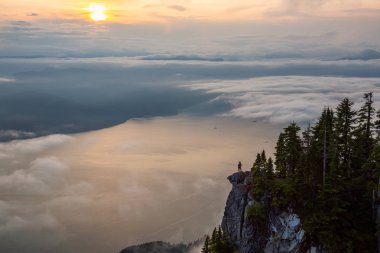 Canlı bir yaz gün batımı sırasında bulutlarla kaplı bir dağın tepesinde Kadın Hiker. St Mark Zirvesi'nin zirvesinde yer aldı, Batı Vancouver, British Columbia, Kanada.