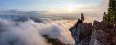 Maceracı Kadın Hiker canlı bir yaz gün batımı sırasında bulutlarla kaplı bir dağın tepesinde. St Mark Zirvesi'nin zirvesinde yer aldı, Batı Vancouver, British Columbia, Kanada.
