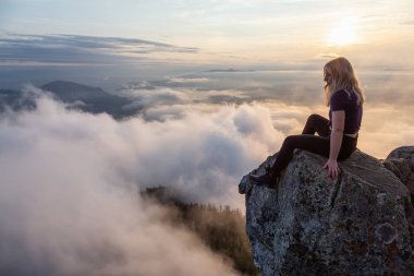 Maceracı Kadın Hiker canlı bir yaz gün batımı sırasında bulutlarla kaplı bir dağın tepesinde. St Mark Zirvesi'nin zirvesinde yer aldı, Batı Vancouver, British Columbia, Kanada.