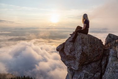 Maceracı Kadın Hiker canlı bir yaz gün batımı sırasında bulutlarla kaplı bir dağın tepesinde. St Mark Zirvesi'nin zirvesinde yer aldı, Batı Vancouver, British Columbia, Kanada.