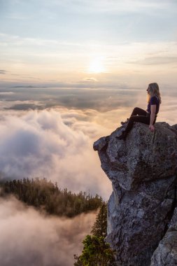 Maceracı Kadın Hiker canlı bir yaz gün batımı sırasında bulutlarla kaplı bir dağın tepesinde. St Mark Zirvesi'nin zirvesinde yer aldı, Batı Vancouver, British Columbia, Kanada.