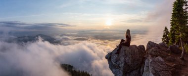 Maceracı Kadın Hiker canlı bir yaz gün batımı sırasında bulutlarla kaplı bir dağın tepesinde. St Mark Zirvesi'nin zirvesinde yer aldı, Batı Vancouver, British Columbia, Kanada.
