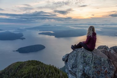 Maceracı Kadın Hiker canlı bir yaz gün batımı sırasında bulutlarla kaplı bir dağın tepesinde. St Mark Zirvesi'nin zirvesinde yer aldı, Batı Vancouver, British Columbia, Kanada.