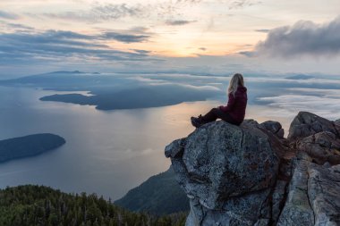Maceracı Kadın Hiker canlı bir yaz gün batımı sırasında bulutlarla kaplı bir dağın tepesinde. St Mark Zirvesi'nin zirvesinde yer aldı, Batı Vancouver, British Columbia, Kanada.