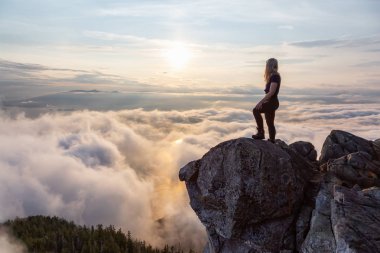 Maceracı Kadın Hiker canlı bir yaz gün batımı sırasında bulutlarla kaplı bir dağın tepesinde. St Mark Zirvesi'nin zirvesinde yer aldı, Batı Vancouver, British Columbia, Kanada.