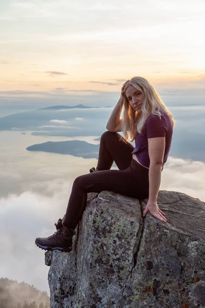 Adventurous Female Hiker on top of a mountain covered in clouds during a vibrant summer sunset. Taken on top of St Mark\'s Summit, West Vancouver, British Columbia, Canada.